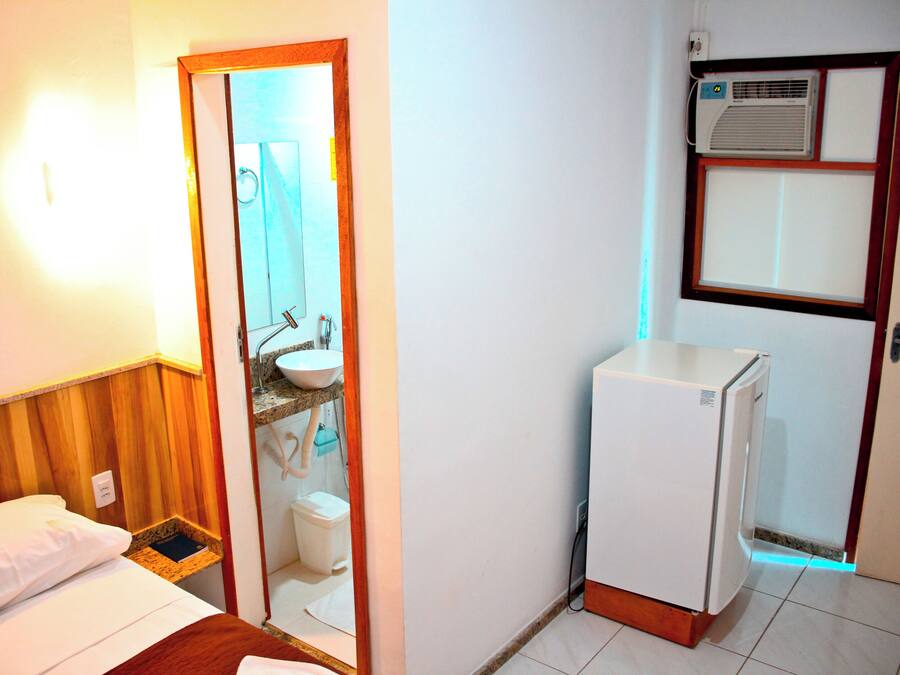 A compact hotel room with a bed, a small bathroom with a sink and toilet, and a white refrigerator.