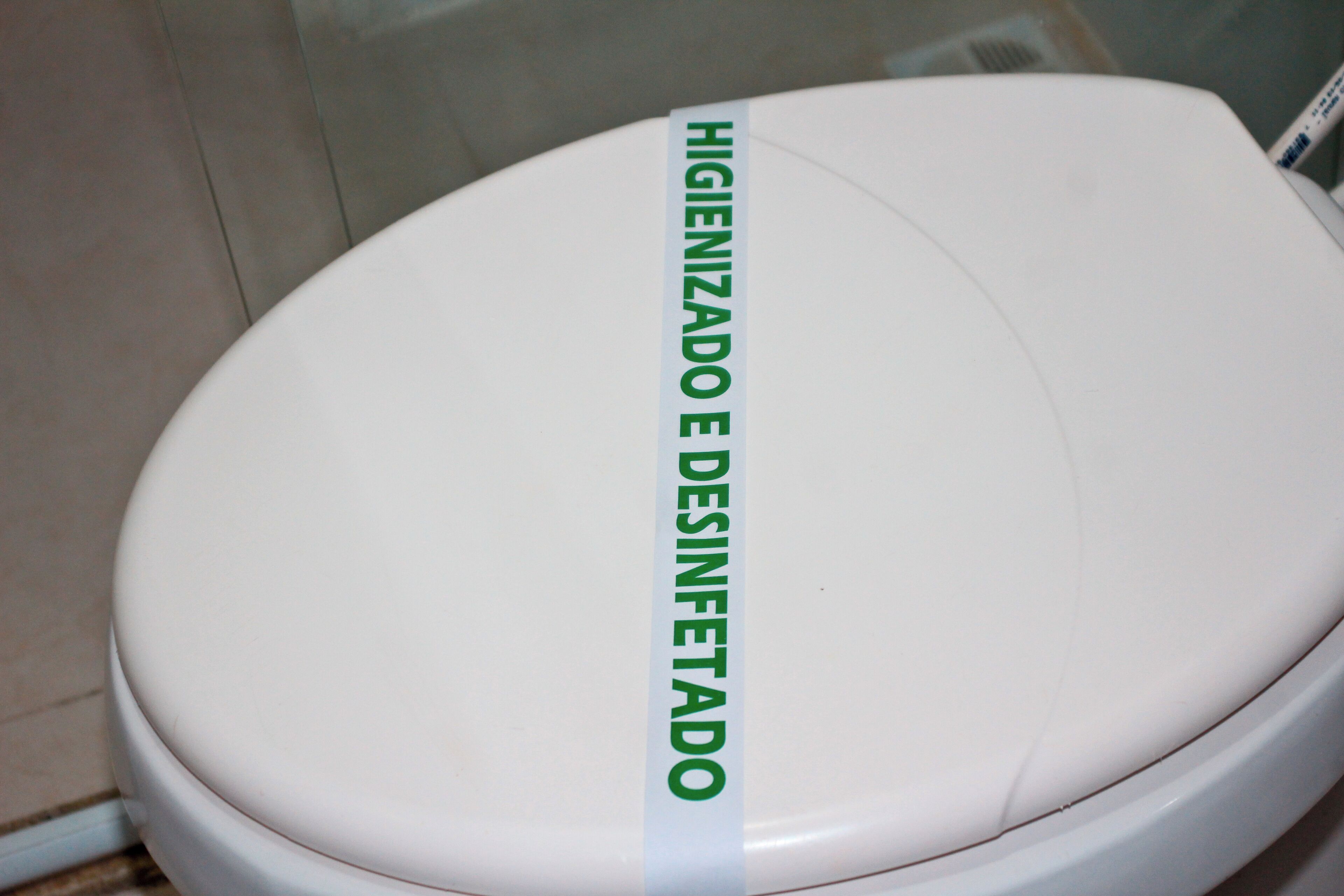 A toilet with a green label that reads "HIGIENIZADO E DESINFETADO".