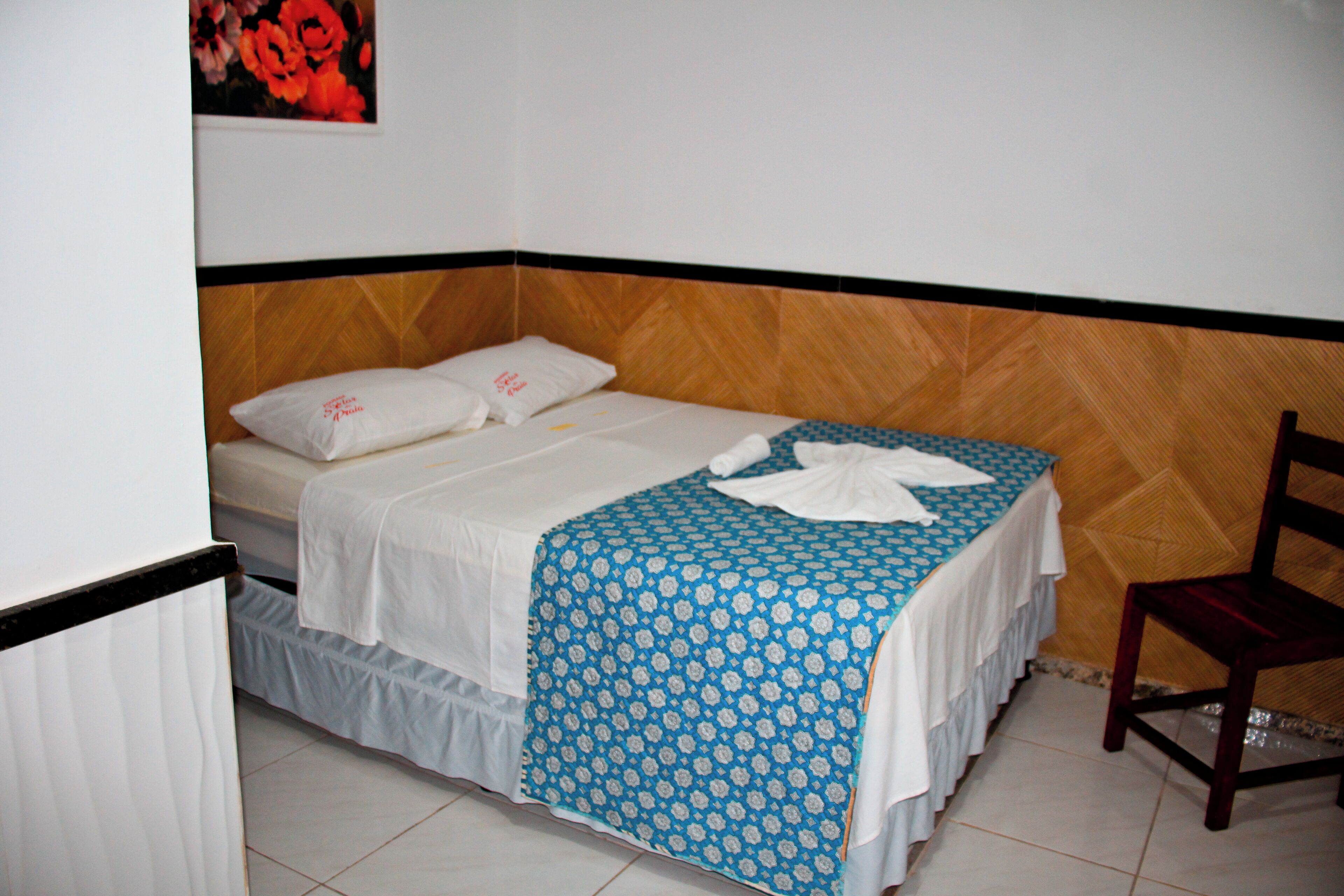 Un letto singolo con copriletto azzurro a motivi decorativi, cuscini bianchi e una testiera in legno.