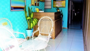 Un espace d’accueil avec un bureau en bois, deux chaises blanches, une grande plante en pot et un tableau encadré accroché au mur.