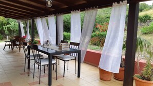 A covered outdoor dining area with a table and chairs, surrounded by potted plants and a view of greenery. - Alghero Rural Relax & Private Comfort Exclusive Villa Laurus (Alghero)