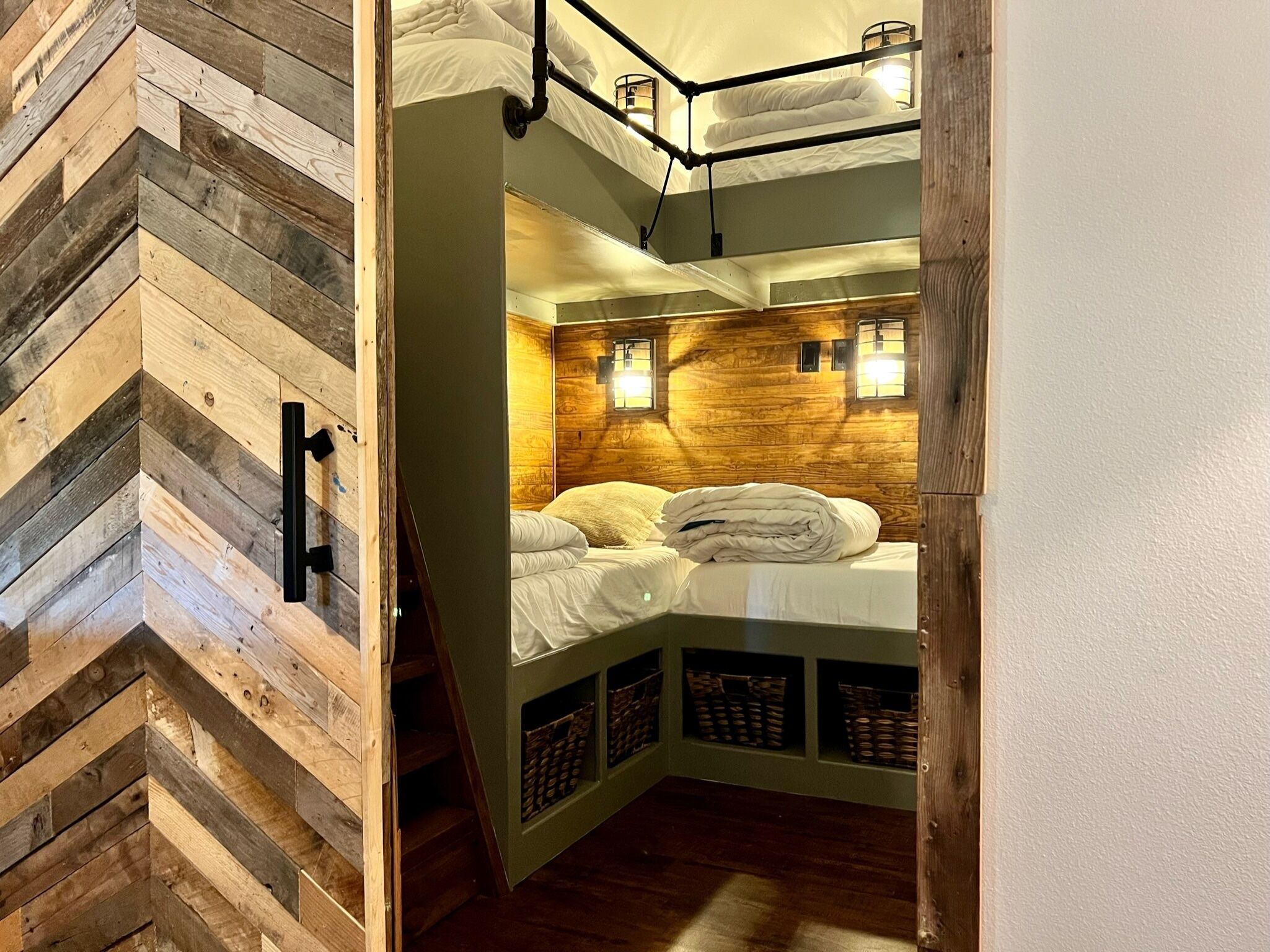 A compact, multi-level room with a herringbone wood wall, a bunk bed, and built-in storage baskets.