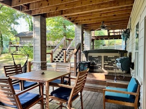 A covered outdoor patio with wooden furniture, a grill, and a staircase leading to a deck.