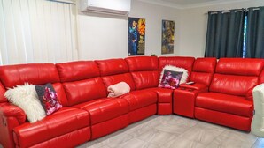 A red leather sectional sofa with a remote control and a white furry throw pillow. - FAMILY HOLIDAY HOME (Redbank Plains)
