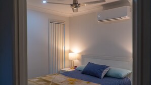 A bedroom with a bed, a nightstand, a lamp, a ceiling fan, and an air conditioning unit. - FAMILY HOLIDAY HOME (Redbank Plains)