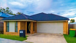 A residential house with a garage, a front yard, and a clear sky. - FAMILY HOLIDAY HOME (Redbank Plains)
