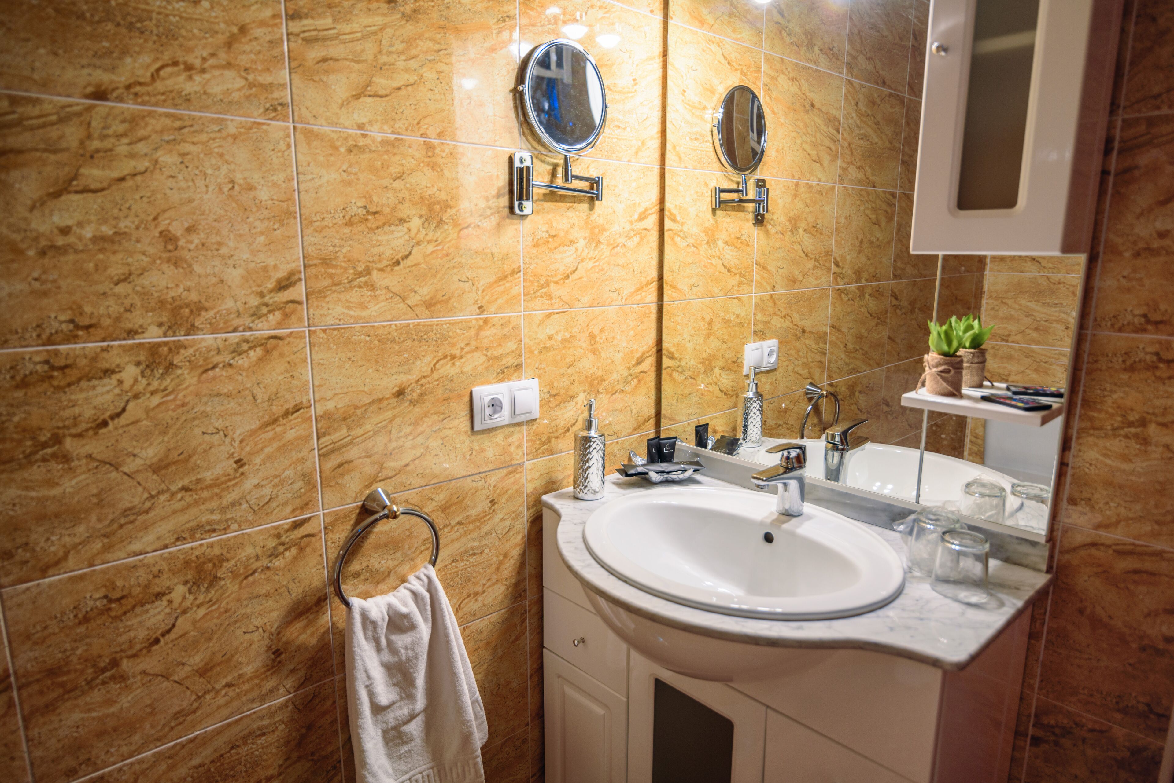 A bathroom with a marble wall, a sink, two mirrors, and a towel rack.