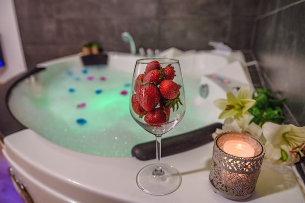 A glass of strawberries on a table with a candle and a bathtub with floating objects.