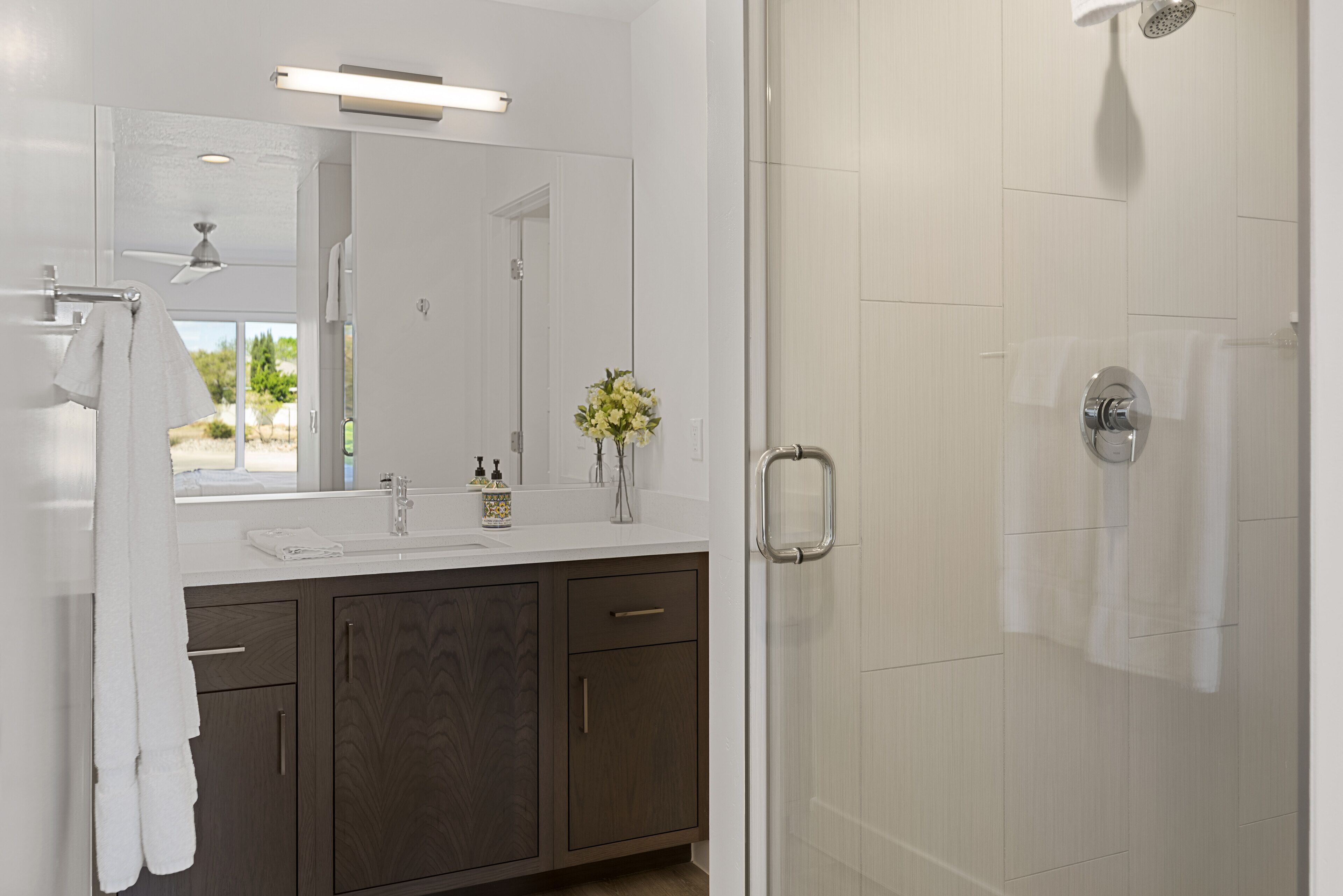 Une salle de bain moderne avec un grand miroir, une douche et un meuble-lavabo doté d’un évier et d’armoires.