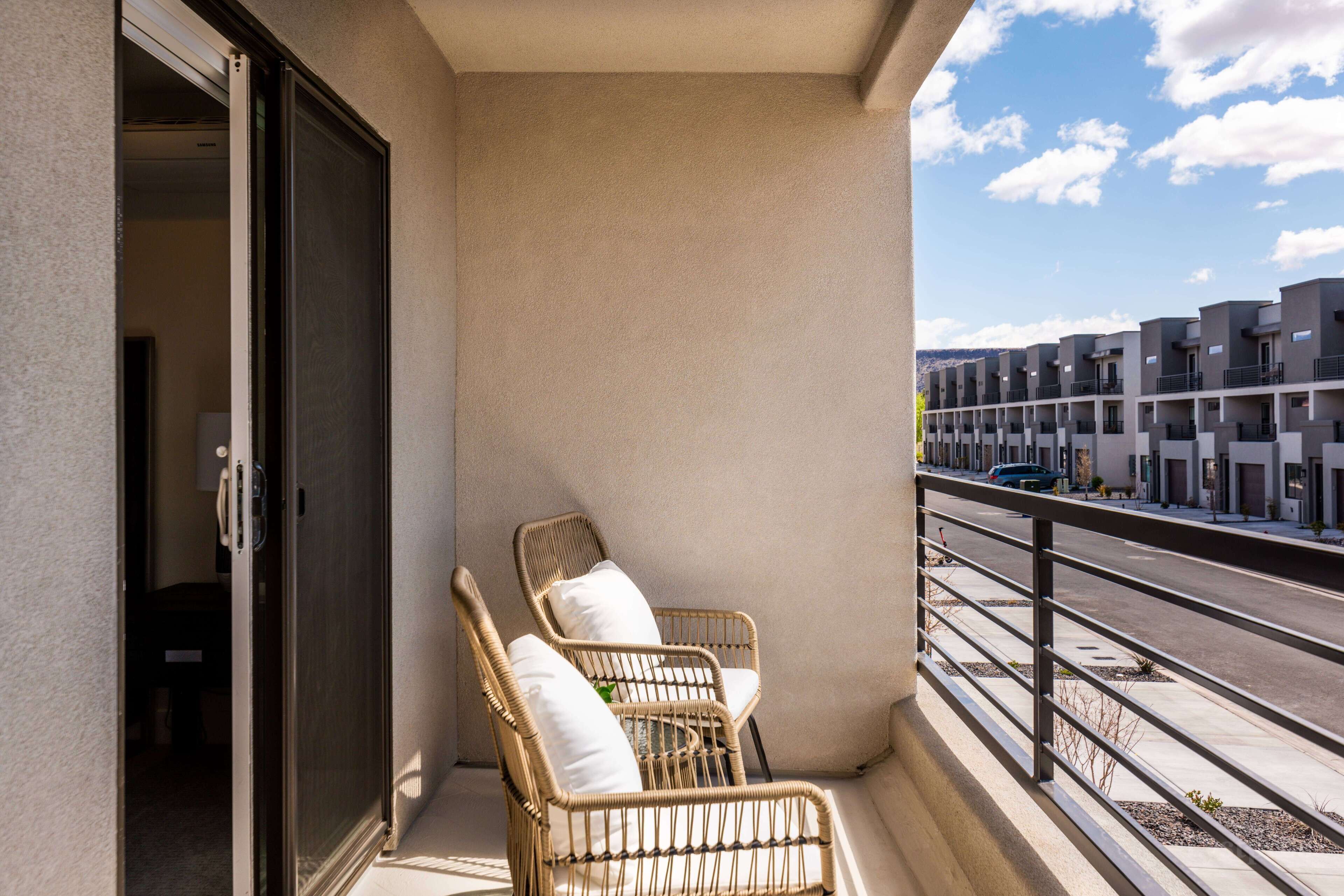 A balcony with wicker chairs and a view of a modern building complex.