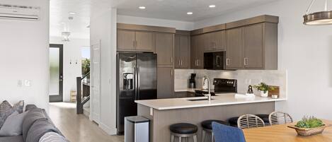 A modern kitchen with stainless steel appliances, a central island, and a dining area with bar stools.