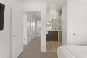 A hotel room with a bed, a bathroom with a sink, and a hallway leading to other rooms.