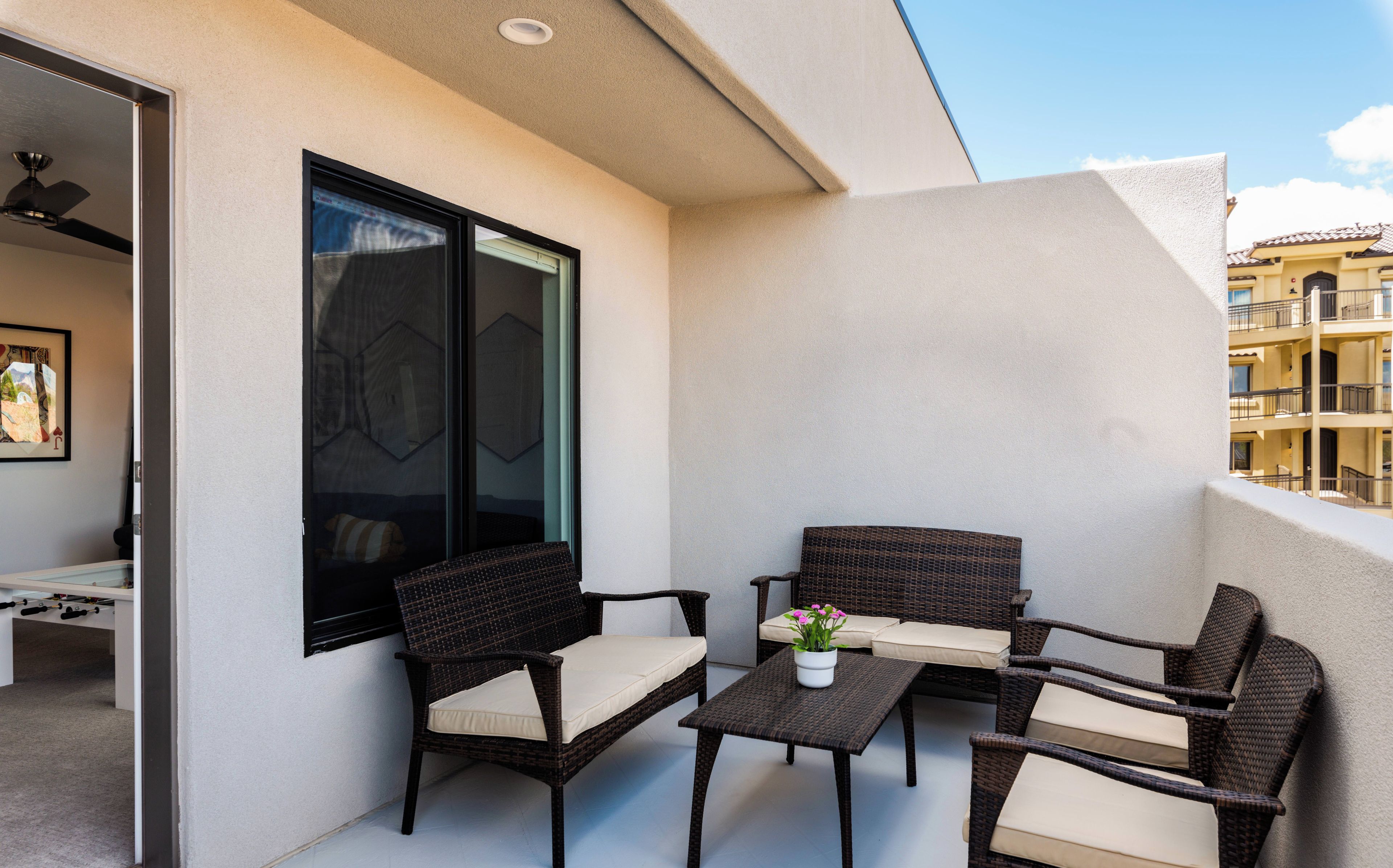 A balcony with wicker furniture, a small table with a flower pot, and a sliding glass door.