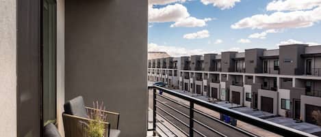 Ein Balkon mit Korbstühlen und einem kleinen Topfpflanzen, mit Blick auf eine Reihe moderner Gebäude und einen klaren Himmel.