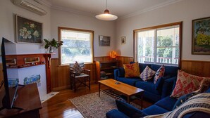 A cozy living room with a blue sofa, wooden coffee table, and a bookshelf. - Moorhead Beach Cottage - Wallaga Lake Rd 60 (Bermagui)