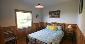 A bedroom with a bed, a bench, a nightstand, a lamp, a window, and a painting on the wall.