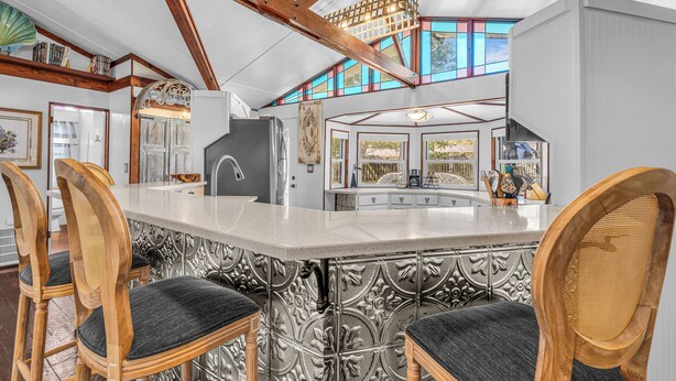 A kitchen with a bar area, wooden chairs, and a large window. - Silo House (Fairhope)