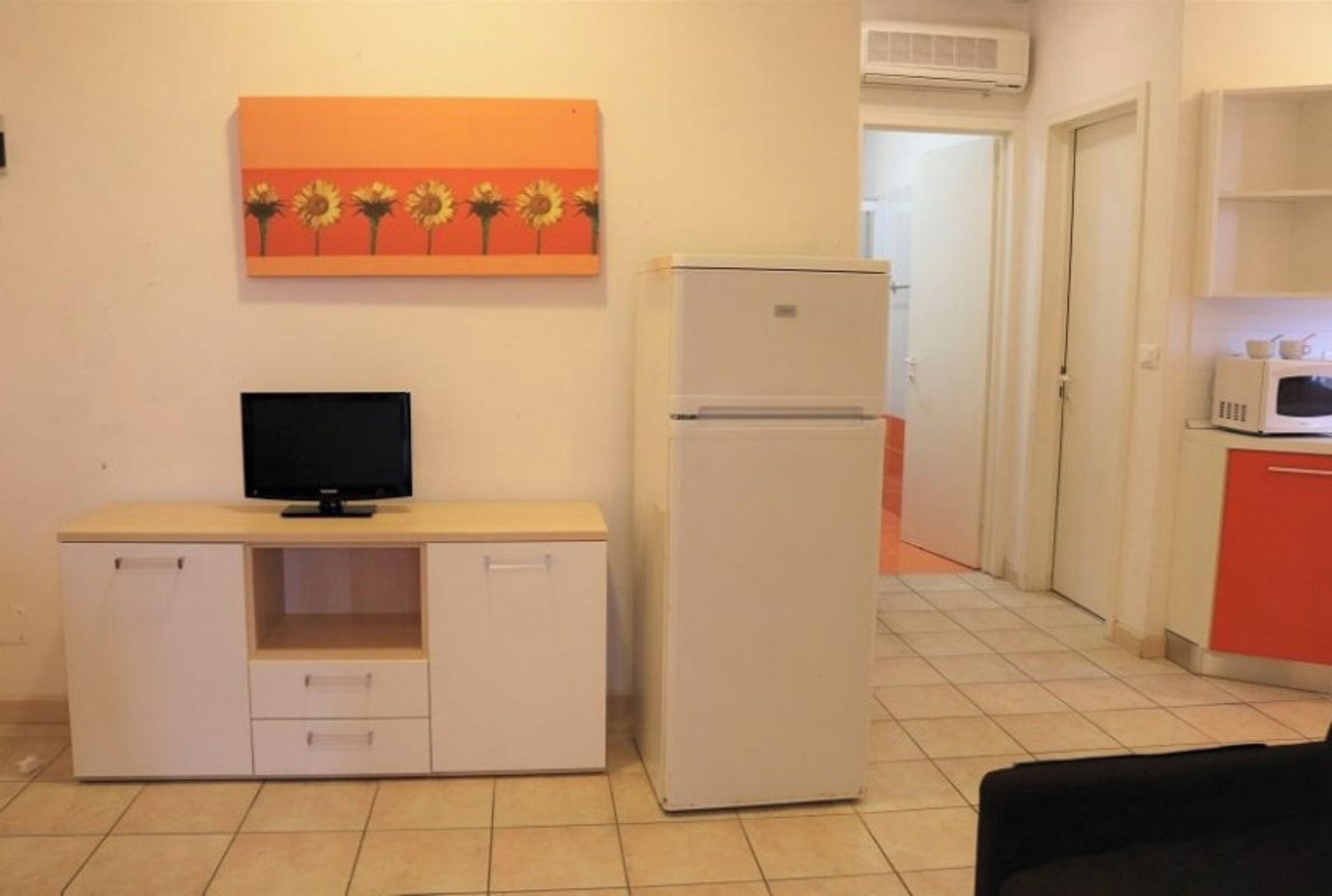 A compact living space with a kitchenette, a flat-screen TV, and a refrigerator.