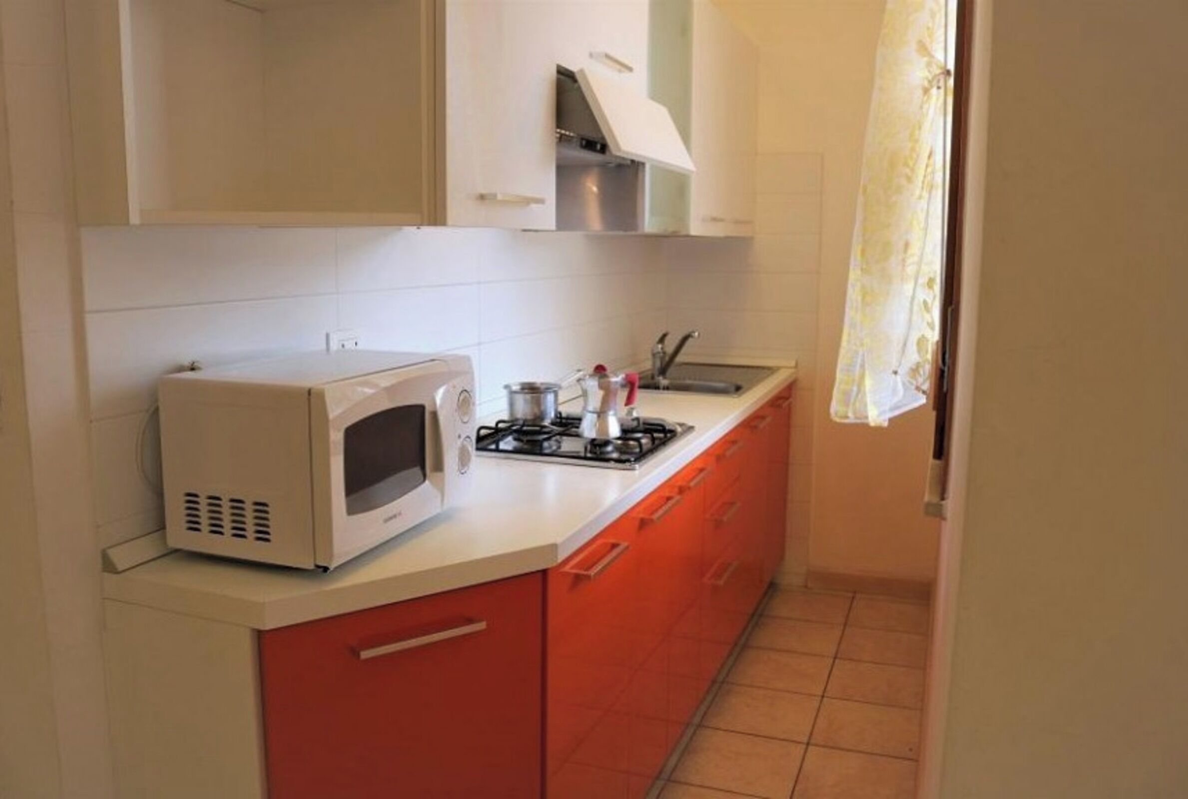 Een kleine keuken met witte kastjes, een magnetron, een gasfornuis en een spoelbak.