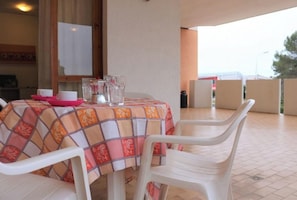 Uma mesa com toalha quadriculada, cadeiras de plástico branco e um jarro de vidro sobre a mesa.