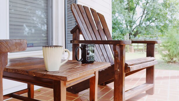 Une table en bois, avec une tasse blanche et une tasse noire portant une inscription, et une chaise en bois dotée d’un dossier.