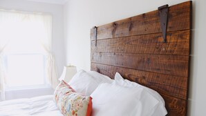 Un lit avec une literie blanche et un coussin à motifs floraux, une tête de lit en bois et une lampe de chevet.