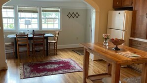Une cuisine avec des meubles de rangement en bois, une table à manger avec des chaises et un tapis rouge.
