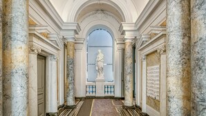 A grand hallway with marble columns, a statue, and a patterned floor.