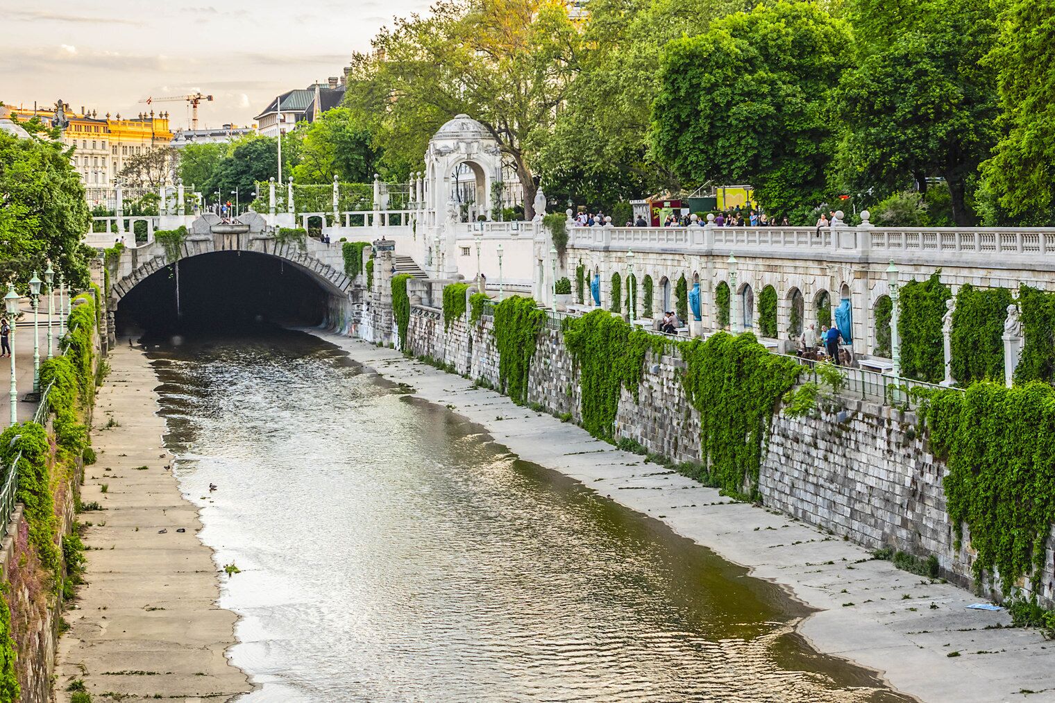A stone bridge with a tunnel entrance, a river, and a stone wall with greenery.