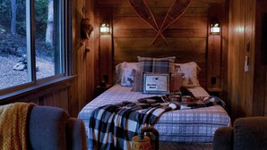 Un dormitorio acogedor con cabaña, una cama grande, dos lámparas de pared y una ventana con vistas a un bosque.