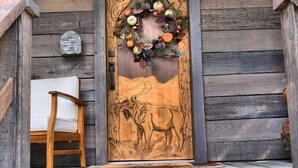 Una puerta de madera con un alce tallado, un adorno y un banco en el exterior.