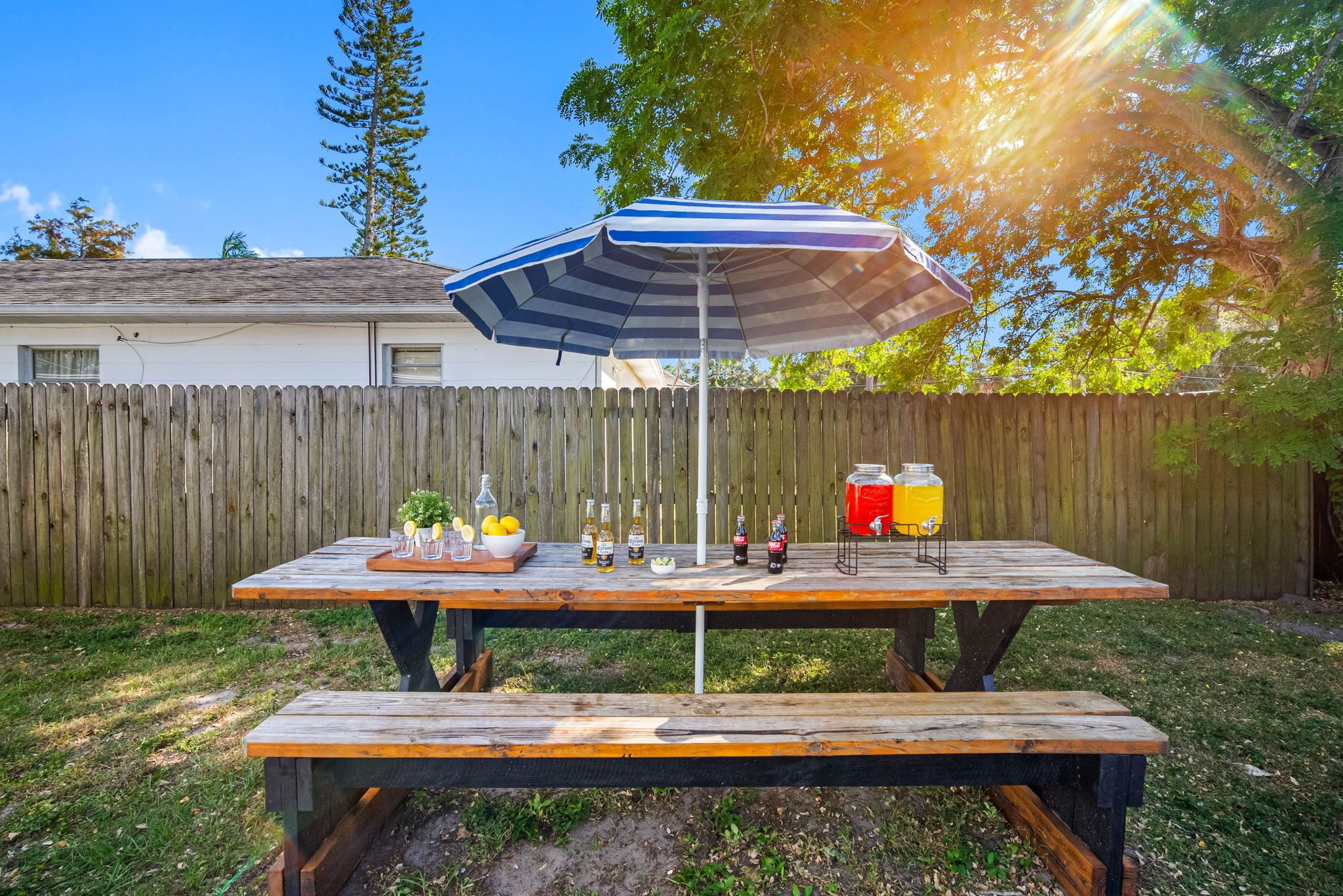Een houten picknicktafel met een gestreepte parasol, omgeven door een houten hek en bomen.