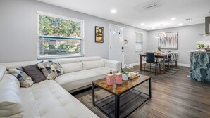 Ein modernes Wohnzimmer mit einem Ecksofa, einem Holztisch und einem Essbereich mit Tisch und Stühlen.