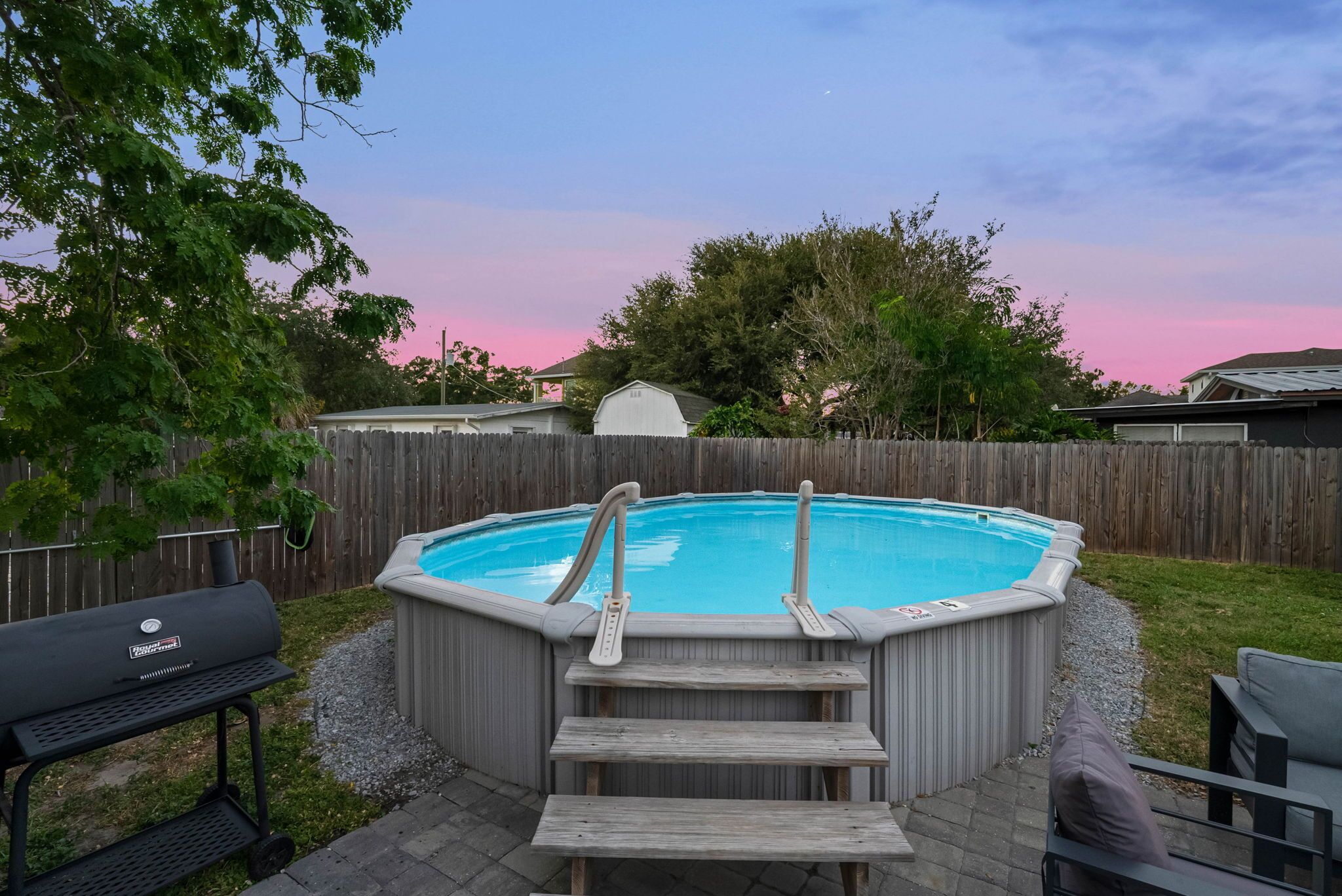 En baghave med jacuzzi, trætrappe, grill og en indhegnet område.