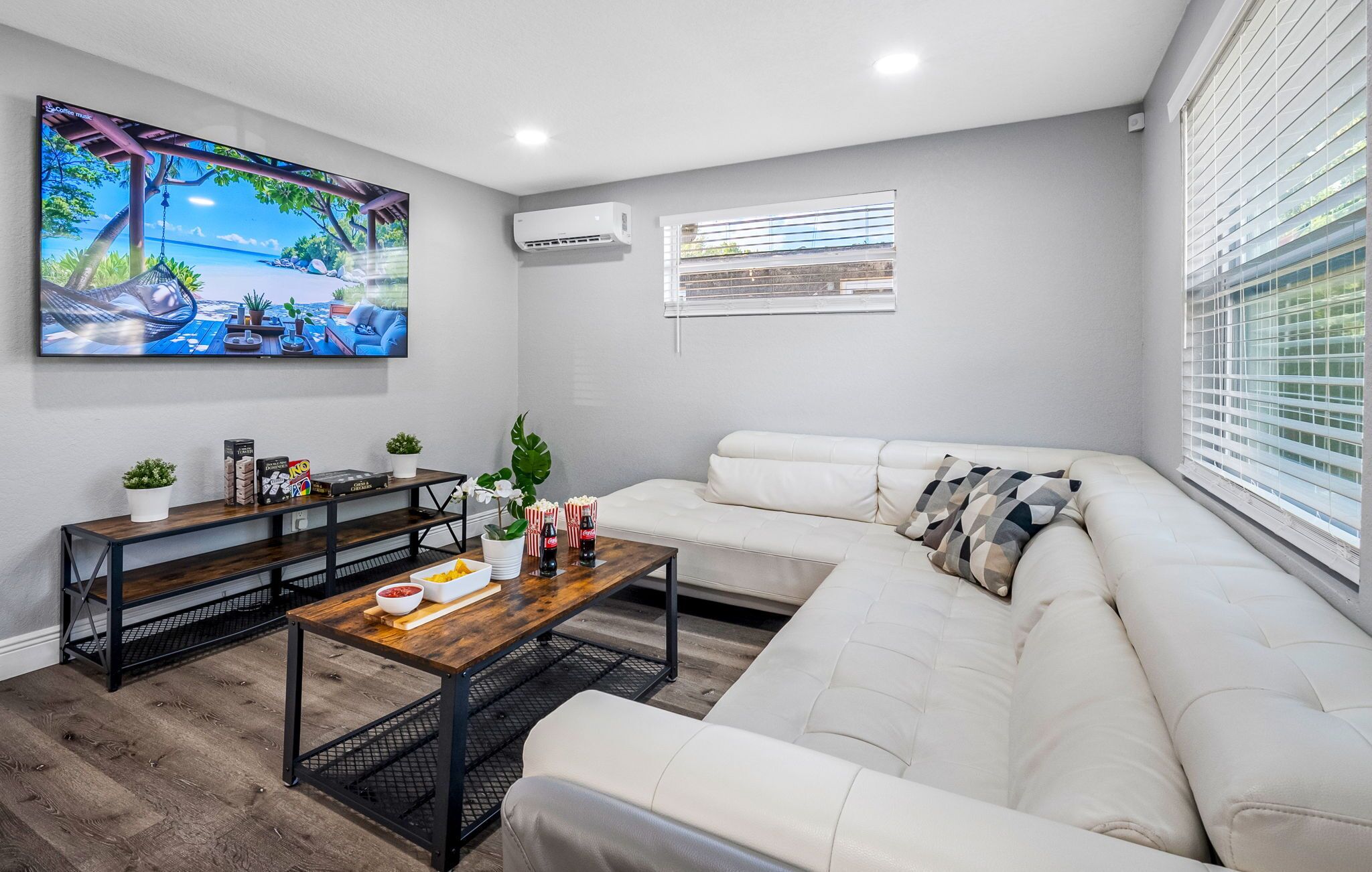 Una sala de estar moderna con un sofá blanco, una mesa de centro de madera y un televisor montado en la pared que muestra una escena tropical.