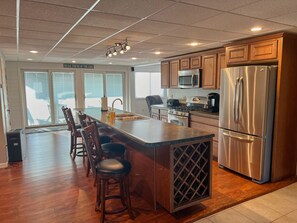 A modern kitchen with wooden cabinets, stainless steel appliances, and a bar area with stools. - Centrally Located in Heart of Sister Lakes, Michigan (Dowagiac)
