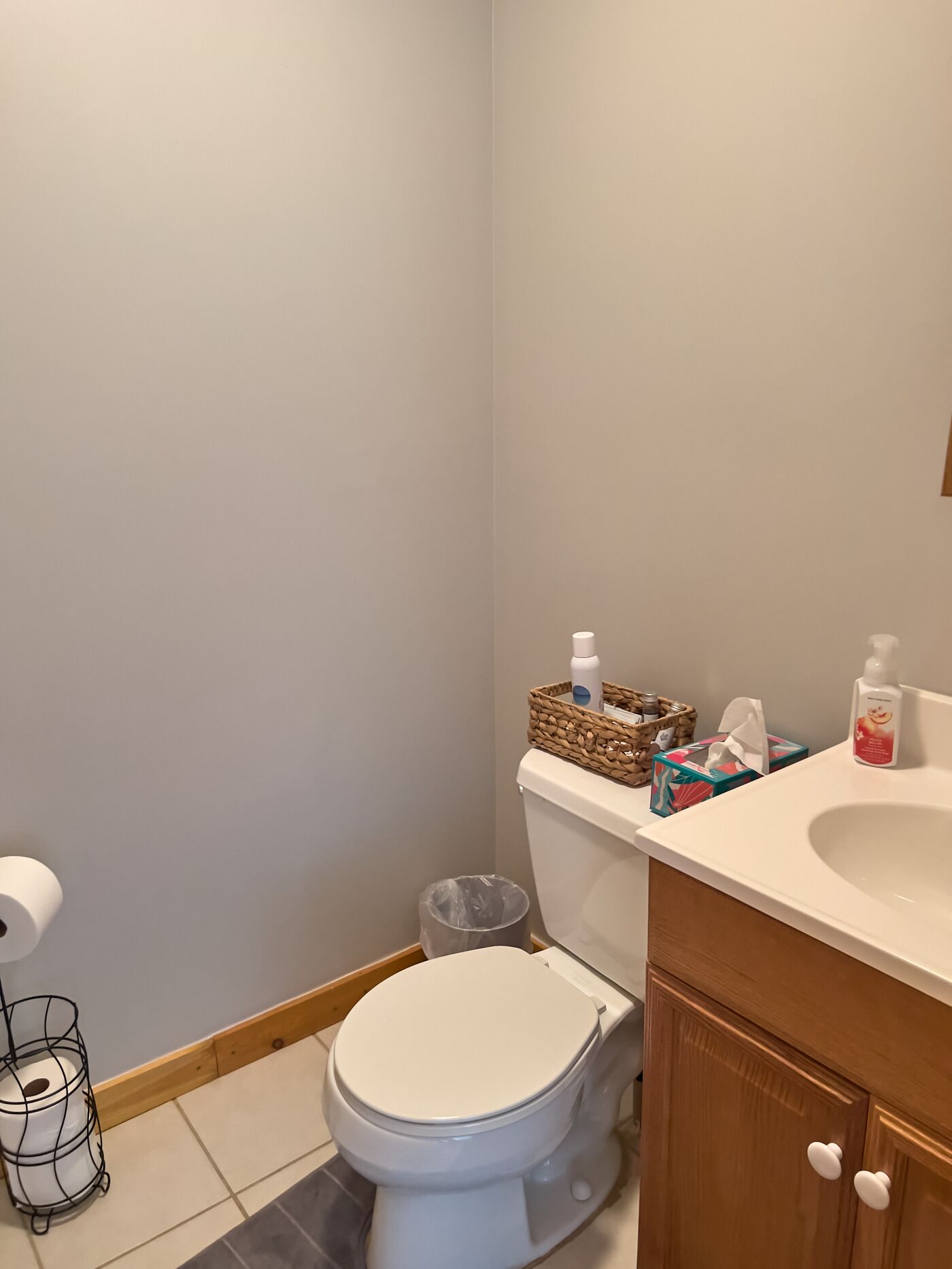 Une salle de bain avec des toilettes, un lavabo et une poubelle. On trouve des articles de toilette sur le comptoir du lavabo.