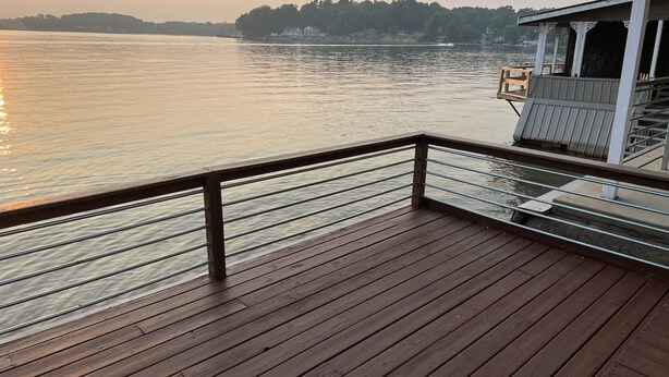 A wooden deck with metal railings overlooking a calm body of water at sunset. - Centrally Located in Heart of Sister Lakes, Michigan (Dowagiac)