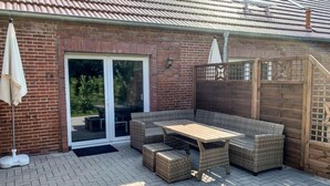 A patio with wicker furniture, a table, and a sliding glass door leading to a garden. - Wangerooge by Interhome (Westerholt)