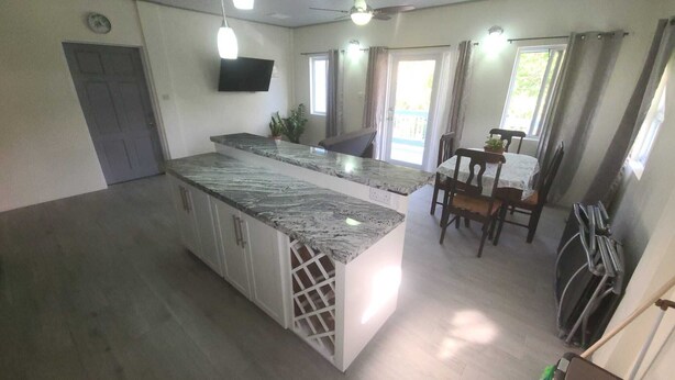 A kitchen with a granite countertop, white cabinets, and a dining area with a table and chairs. - Tranquil Suites - Feels like home (Choiseul)