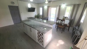 Een keuken met een granieten aanrecht, witte kasten, en een eethoek met een tafel en stoelen.