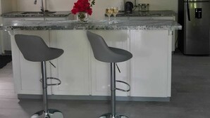 A modern kitchen with white cabinets, a stainless steel refrigerator, two bar stools, and pendant lights. - Tranquil Suites - Feels like home (Choiseul)