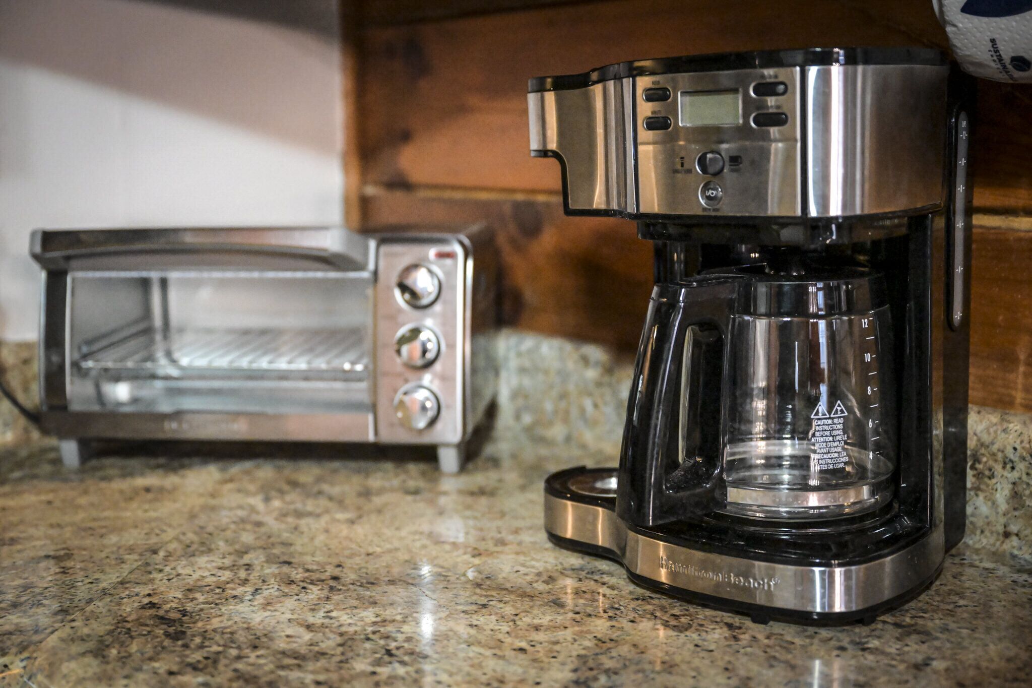A coffee maker with a glass carafe and a toaster on a granite countertop.