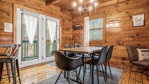 A wooden cabin interior with a dining table, chairs, and a chandelier.
