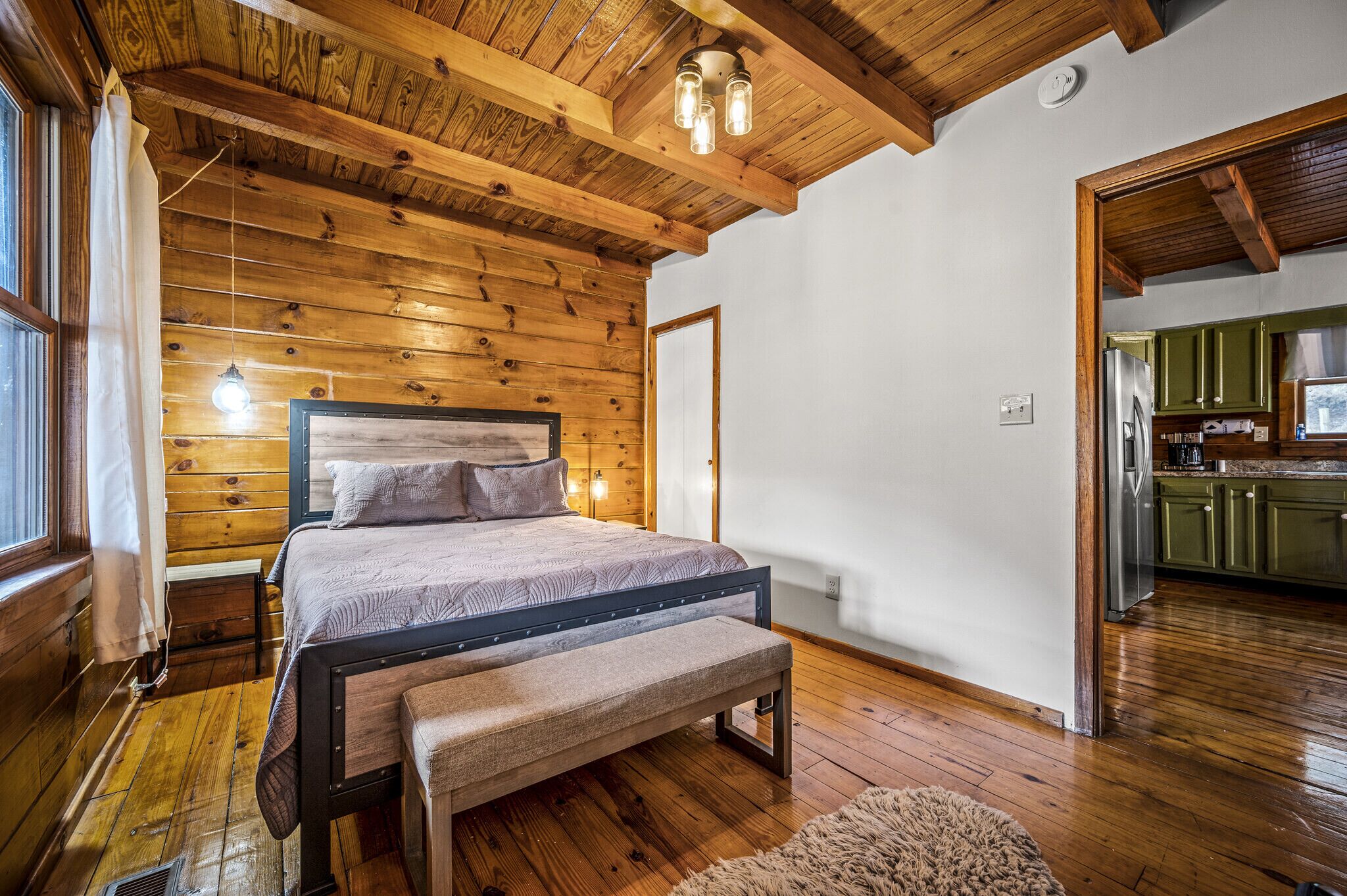 Un dormitorio con paneles de madera, una cama, un banco y una lámpara colgante.
