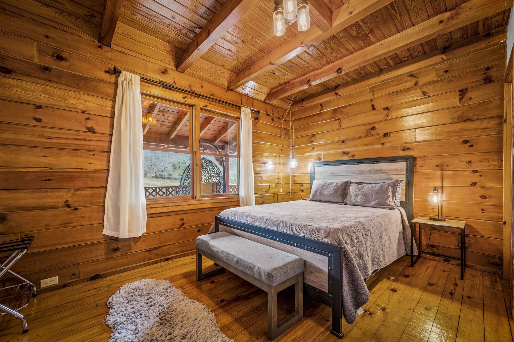 Une chambre dans une cabane en bois, avec un lit, un banc et une petite table sur laquelle se trouve une lampe.