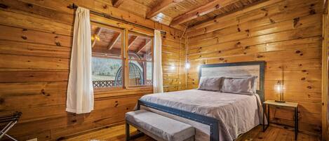 A wooden cabin bedroom with a bed, bench, and a small table with a lamp.