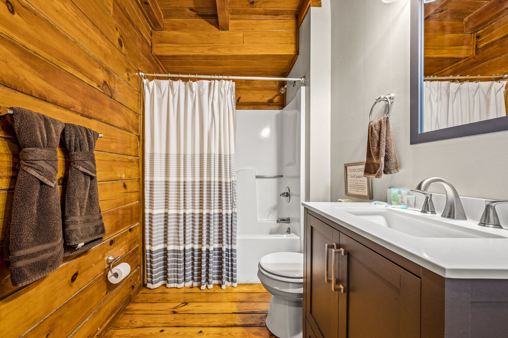 A wooden-paneled bathroom with a shower, toilet, and sink.