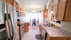 A modern kitchen with wooden cabinets, stainless steel appliances, and a dining area with a table and chairs. - Beautiful Home in Golf Course Community - 3 Bedroom plus Den (Meridian)