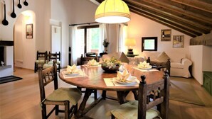 Zona de dinar amb taula de fusta preparada per a quatre persones, envoltada de cadires amb coixins. Damunt la taula hi penja una gran làmpada penjant groga.